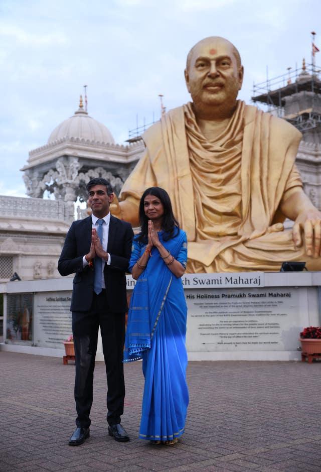 Rishi Sunak and his wife, Akshata Murty, stand in front of a statue
