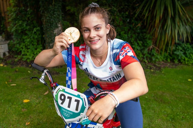 Beth Shriever leans on her bike with a gold medal in her hand
