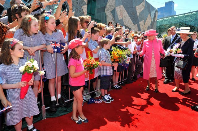 Queen Elizabeth II smiles as she is given flowers by two young girls in Federation Square, Melbourne, during a walk-about in the south Australian city