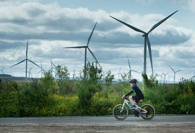 A child rides a bike past three wind turbines