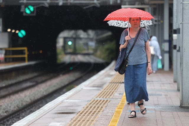 A woman walks along a train platform carrying an umbrella