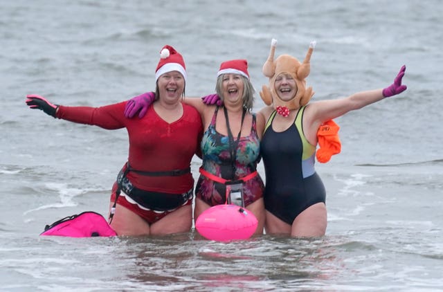 Three female swimmers in Christmas fancy dress pose for a photo in the sea off Cullercoats Bay in North Tyneside