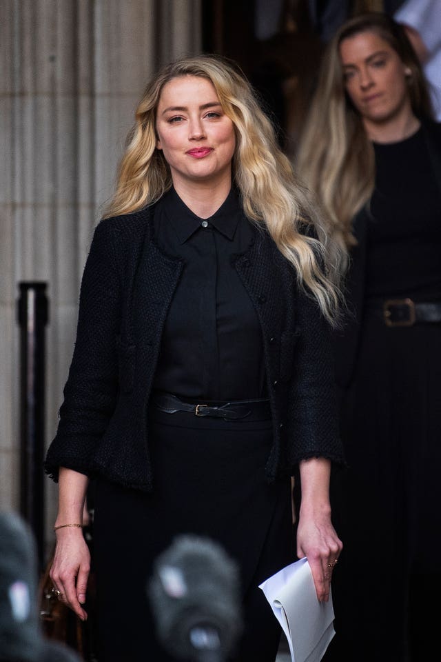 Amber Heard in black outfit holding sheaf of papers