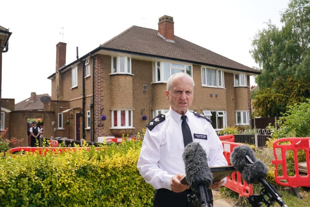 Chief Superintendent Sean Wilson standing at a pair of microphones in front of a semi-detached house.