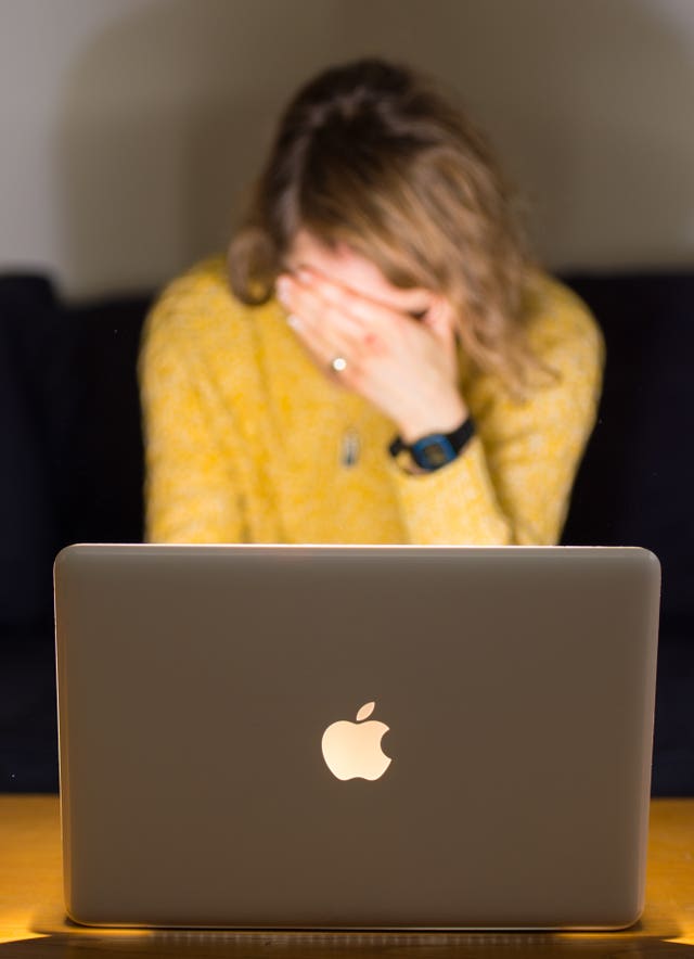 A woman holds a hand to her face in front of an open laptop