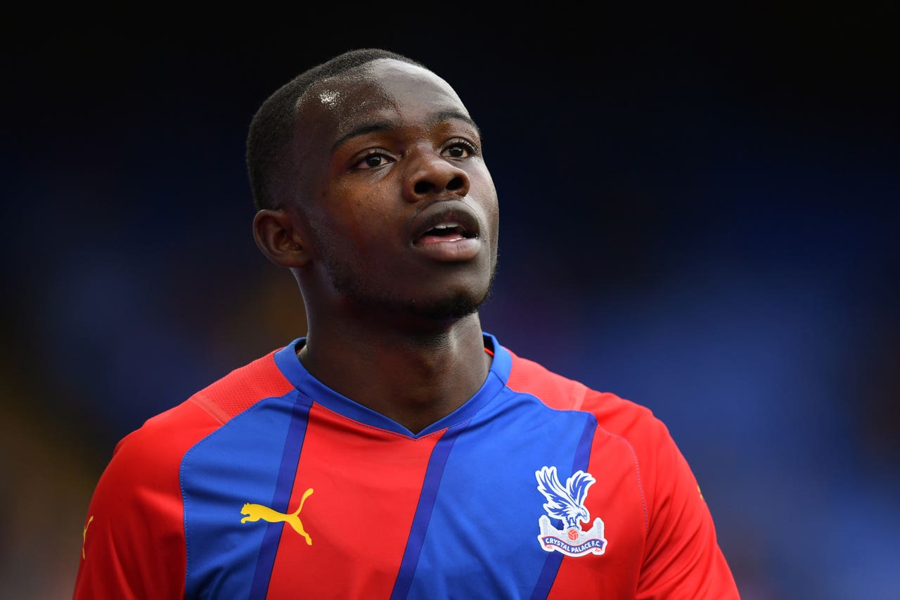  A young male football player, Tyrick Mitchell, is playing a match for his team, Crystal Palace, wearing a red and blue jersey.