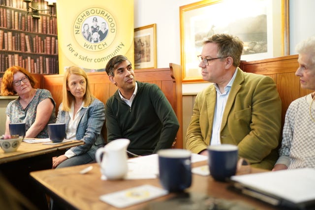 Rishi Sunak talks to people in a pub behind a table with mugs and a milk jug