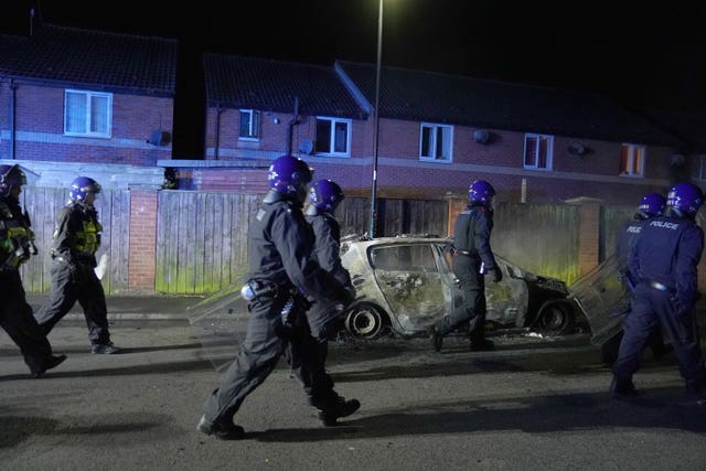 Police Officers walk past a burnt out police vehicle as they are deployed on the streets of Hartlepool following a violent protest