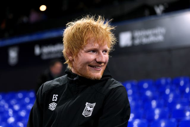 Ed Sheeran laughs as he looks in the opposite direction of the camera at Portman Road