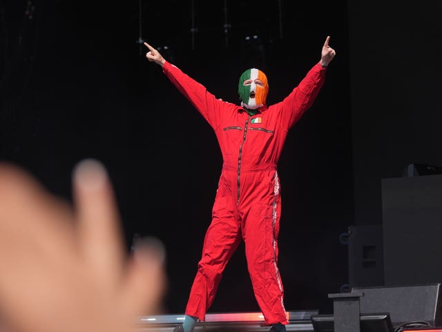 Kneecap member DJ Provai signals to the crowd on the West Holts Stage