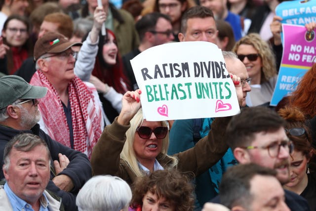 A woman holding a sign saying 'racism divides Belfast unites' 