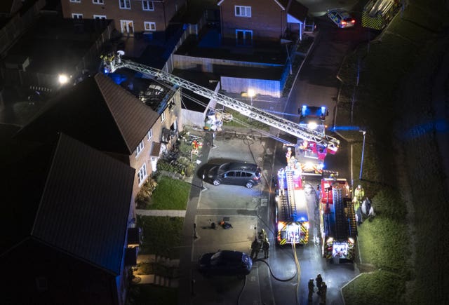 View from above of a home damaged by fire, with firefighters on an aerial ladder