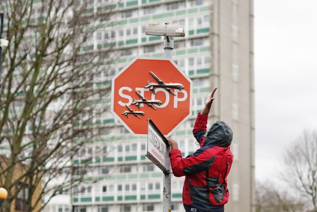 A Banksy artwork of a stop sign with drones on it as a man in red reaches up to it