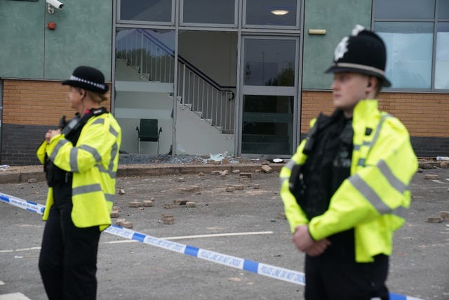 Two police officers outside a building with bricks on the ground behind police tape