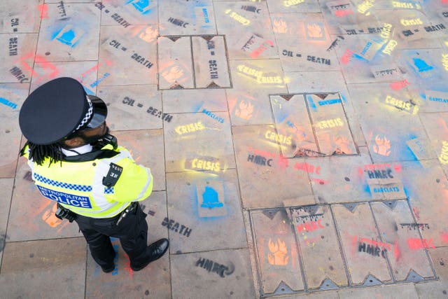 A police officer stands among slogans sprayed onto the pavement outside the offices of HM Revenue and Customs 