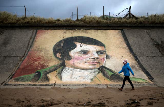 A person walks past a mural of Robert Burns on the sea wall at Ardeer beach