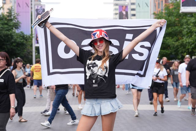 An Oasis fan holds a banner and poses for a photo on Wembley Way, ahead of the first night of the Oasis Live ’25 tour opening at Wembley Stadium in London