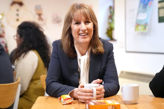 Rachel Reeves smiling, while sitting at the table with her hands wrapped round a mug