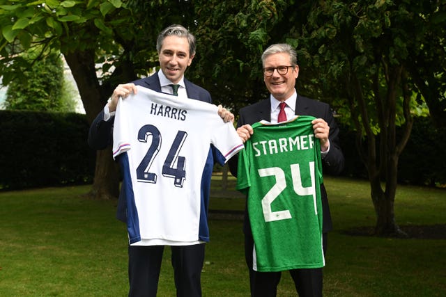 Simon Harris holding up an England football jersey with Harris and the number 24 on the back of it, while Sir Keir Starmer holds up an Ireland football jersey with Starmer 24 on the back