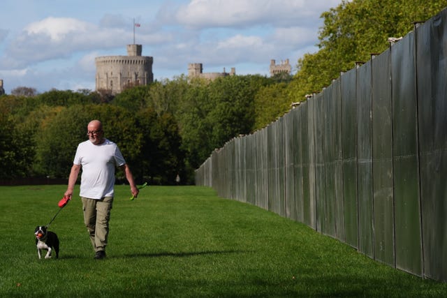A person walks their dog alongside security fencing that has been installed on the Long Walk outside Windsor Castle in Berkshire 
