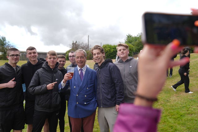 Nigel Farage poses for a selfie with a pint in his hand while flanked by a group of young men