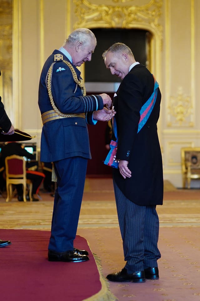 The King pins an honour to the chest of a man wearing a morning suit and sash 