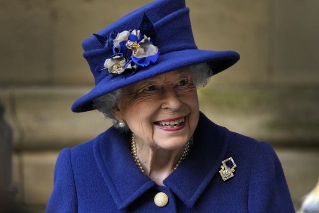 Head and shoulders shot of Queen Elizabeth II smiling, while wearing a dark blue coat and matching hat