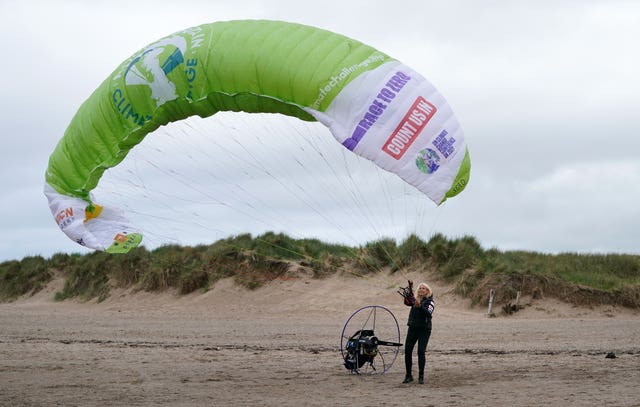 Sacha Dench on a beach, holding her parachute, which is inflated in the air