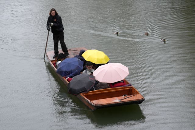 People shelter from the rain under umbrellas as they punt along the River Cam in Cambridge