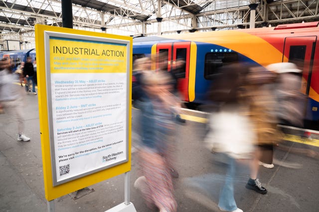 Passengers walk past a display board at Waterloo train station in London