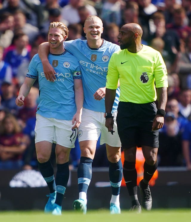 Manchester City striker Erling Haaland puts his arm around Kevin De Bruyne's shoulder alongside referee Sam Allison