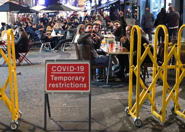 People eating and drinking in Soho, central London, next to a sign warning of Covid-19 restrictions (Yui Mok/PA)