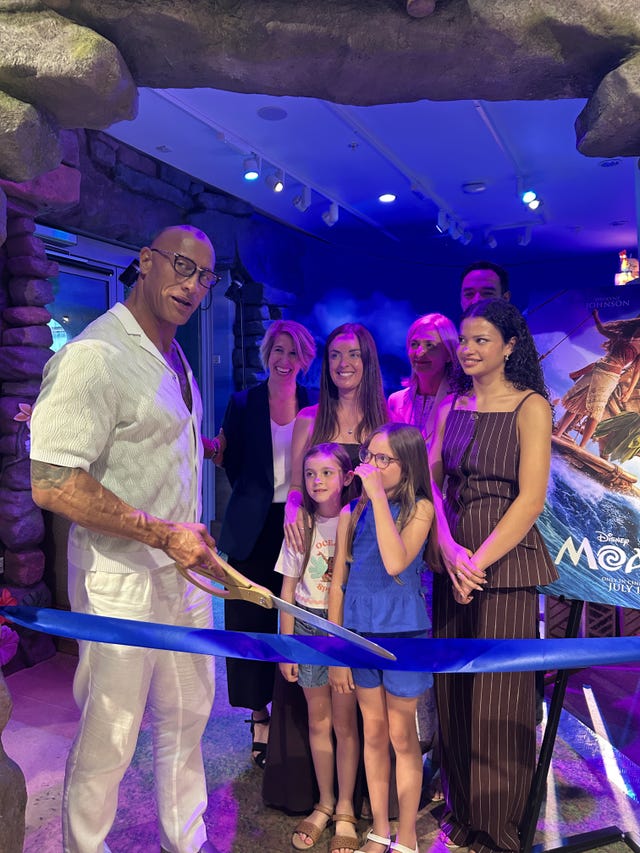Dwayne Johnson cutting a ribbon while Bella, Luna and others look on