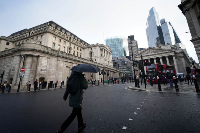 An exterior view of the Bank of England, with a commuter using an umbrella crossing a road in the foreground