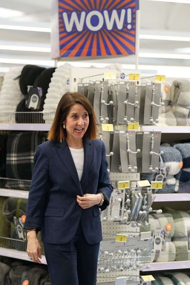 Work and Pensions Secretary Liz Kendall, wearing a navy suit and white top, during a visit to a B&M shop in Bedford, with an orange, blue and white shop sign reading 'Wow!' in the background above her