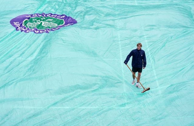 A member of the ground staff sweeps water off the covers 