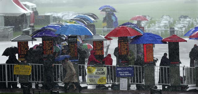 Racegoers try to keep dry as heavy rain falls during a race meeting at York Racecourse (John Giles/PA)