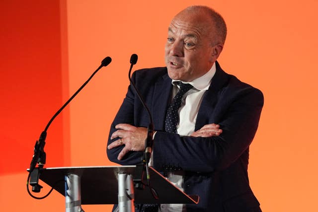 Mike Kane speaking from a lectern, with an orange background