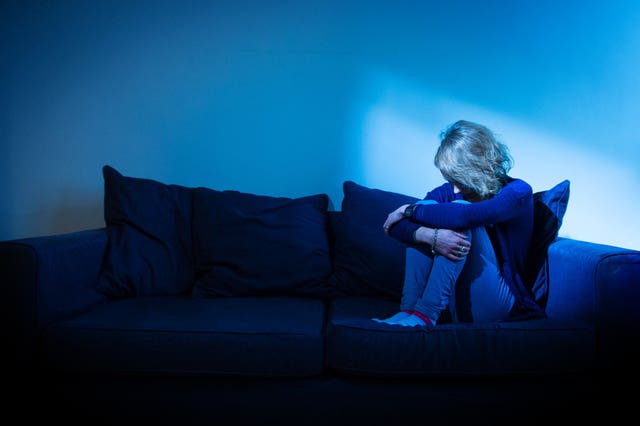 Distressed woman sitting on a sofa, with her head resting on her knees