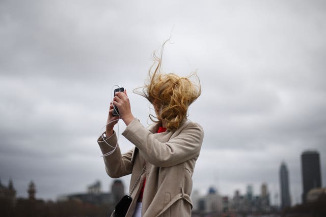 A tourist takes a photograph during strong winds on Westminster Bridge