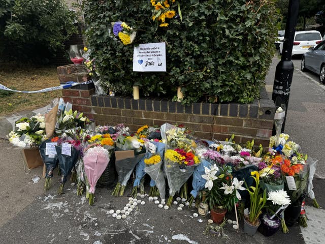 Floral tributes and candles left against a wall, with police tape nearby