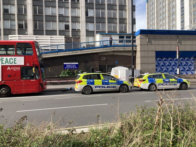 Two parked police cars and a red double decker bus with a forensic tent in the background.