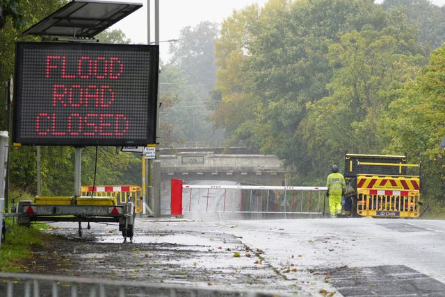 A warning sign on a road in Liverpool as a worker stands near a barrier ahead of a flooded area