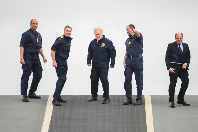 (Left to right) Captain Angus Essenhigh, First Sea Lord Admiral Tony Radakin, Prime Minister Boris Johnson, Commodore Steve Moorhouse and Defence Secretary Ben Wallace face strong winds as they walk on the flight deck