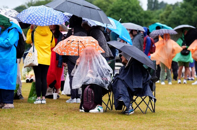 Spectators queue in rain ponchos under umbrellas on Monday morning