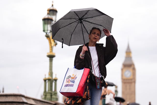 A woman uses an umbrella while walking outside, with the Houses of Parliament in the background