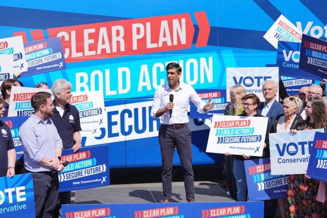 Rishi Sunak delivers a speech in front of a large blue campaign battle bus