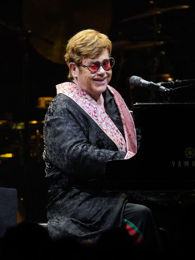 Sir Elton John smiling in heart-shaped sunglasses while playing the piano