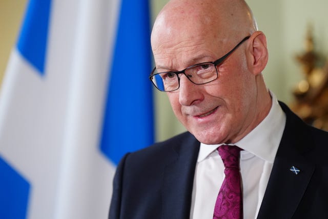 John Swinney speaking in front of a Scottish flag