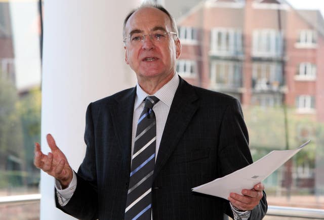 A man in a dark suit holds a sheaf of papers